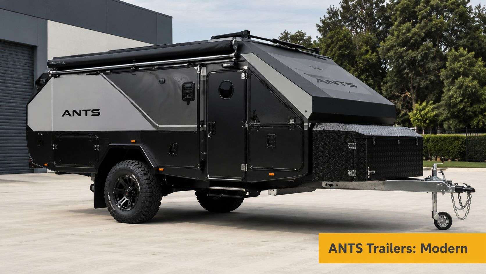 A sleek modern black and grey ANTS off-road camping trailer parked on a concrete lot.
