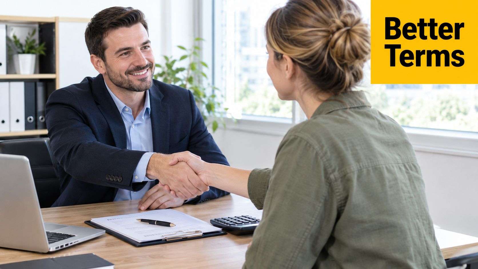 A professional man and woman shaking hands across an office desk after finalizing a business agreement.